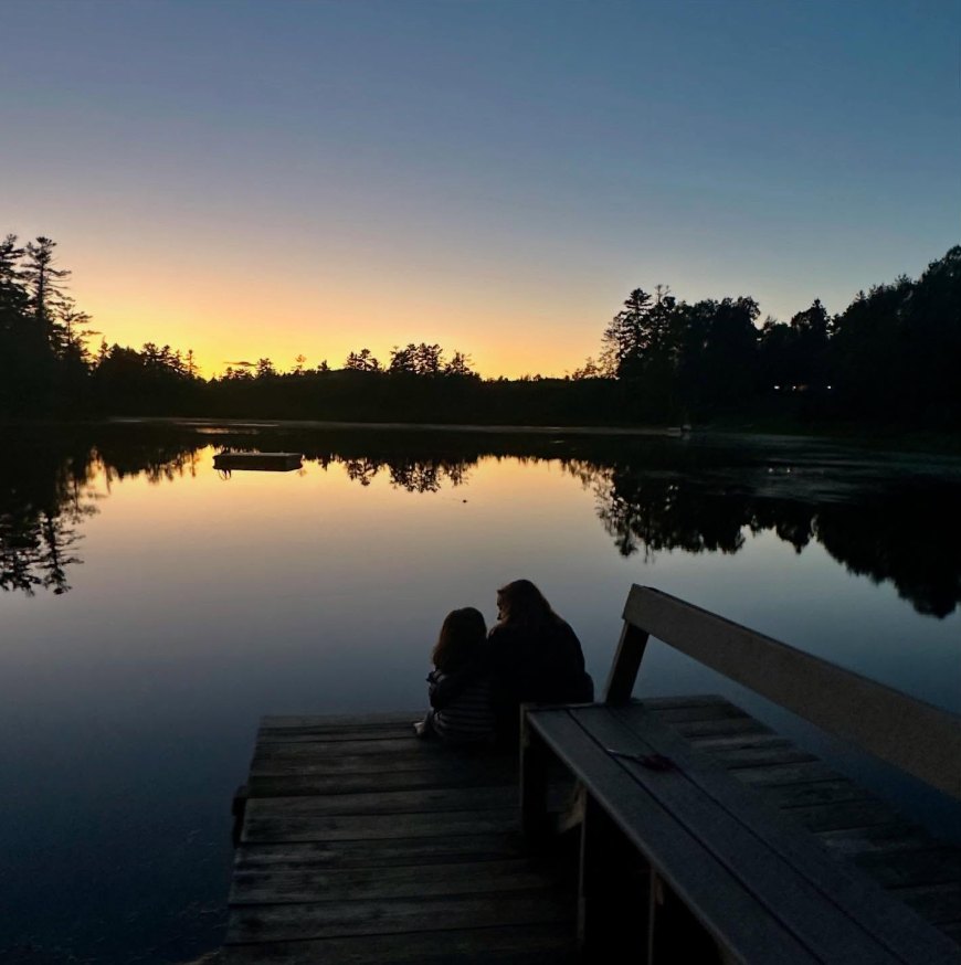 Two silhouettes on a dock at sunset over a still lake